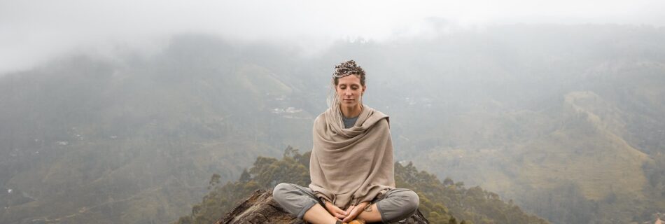 Femme pratiquant le yoga dans un champ verdoyant avec vue sur les montagnes du Queyras.